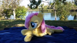 Size: 3264x1836 | Tagged: safe, artist:joltage, character:fluttershy, species:pegasus, species:pony, blanket, crossed legs, female, irl, lake, lying down, outdoors, photo, plushie, solo