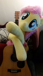 Size: 1836x3264 | Tagged: safe, artist:joltage, character:fluttershy, species:pegasus, species:pony, acoustic guitar, cute, female, guitar, happy, irl, musical instrument, photo, pillow, plushie, smiling, solo