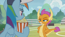 Size: 1366x768 | Tagged: safe, screencap, character:rainbow dash, character:smolder, species:dragon, species:pegasus, species:pony, episode:2-4-6 greaaat, bleachers, clothing, coaching cap, displeased, dragoness, fangs, female, fence, field, flag, folded wings, food, glare, hands on hip, hat, horns, looking at each other, mare, multicolored hair, narrowed eyes, popcorn, raised eyebrow, smolder is not amused, teacher and student, teenaged dragon, teenager, unamused