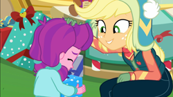 Size: 1922x1080 | Tagged: safe, screencap, character:applejack, character:lily longsocks, equestria girls:holidays unwrapped, g4, my little pony:equestria girls, canterlot mall, child, clothing, cute, dawwww, duo, duo female, female, gift box, gift giving, hat, present, sweet dreams fuel, vest, wholesome, winter break-in, winter hat, winter outfit
