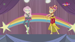 Size: 1136x638 | Tagged: safe, screencap, character:fluttershy, character:sunset shimmer, equestria girls:dance magic, g4, my little pony:equestria girls, alternate hairstyle, awkward smile, ballet slippers, canterlot high, clothing, dress, duo, female, high heels, rainbow, shoes, skirt, stars, teletoon, tutu