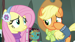 Size: 1280x720 | Tagged: safe, screencap, character:applejack, character:fluttershy, species:pony, episode:best gift ever, g4, my little pony: friendship is magic, clothing, denim jacket, doll, earmuffs, hat, holly the hearths warmer doll, jacket, plastic, scarf, shoddy workmanship, smell, something fishy, sweater, toy