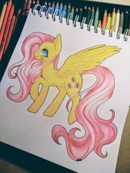 Size: 3120x4160 | Tagged: safe, artist:hikarinohibana, character:fluttershy, species:pegasus, species:pony, g4, blushing, colored pencil drawing, female, mare, pencil, photo, profile, raised hoof, raised leg, sketchpad, smiling, solo, spread wings, standing, traditional art, wings