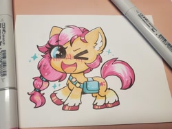 Size: 2048x1536 | Tagged: safe, artist:confetticakez, character:sunny starscout, species:earth pony, species:pony, g5, blushing, chibi, coat markings, colored hooves, copic, cute, cutie mark, eye clipping through hair, eyebrows, eyebrows visible through hair, female, hooves, mare, marker drawing, one eye closed, one hoof raised, open mouth, photo, saddle bag, socks (coat marking), solo, sunny's buttons, sunnybetes, tail, traditional art, unshorn fetlocks, wink